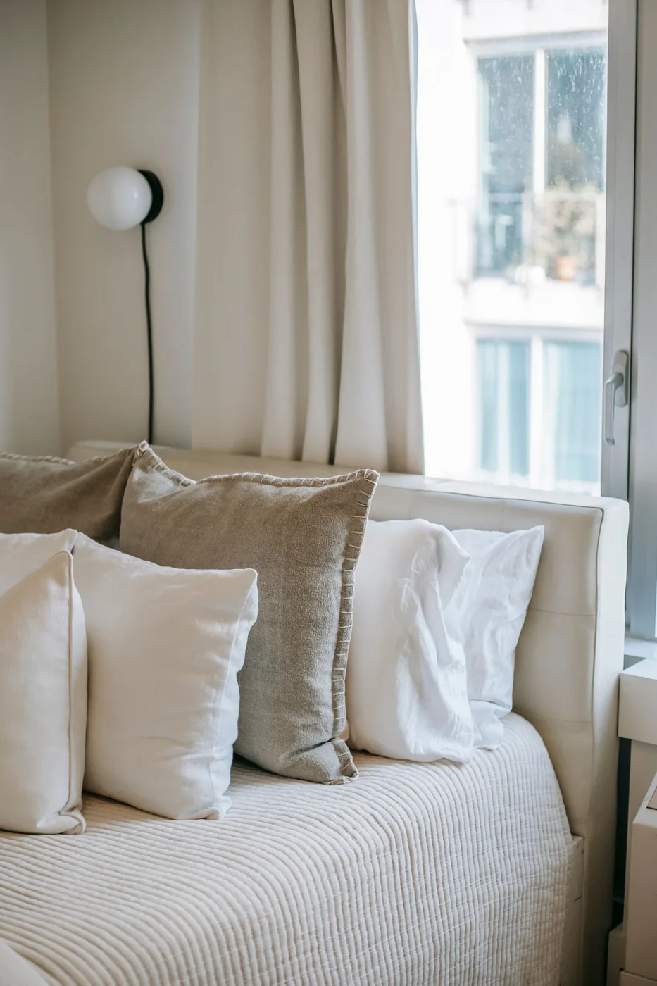 Soft linen cushions and bedding beside a sunlit window