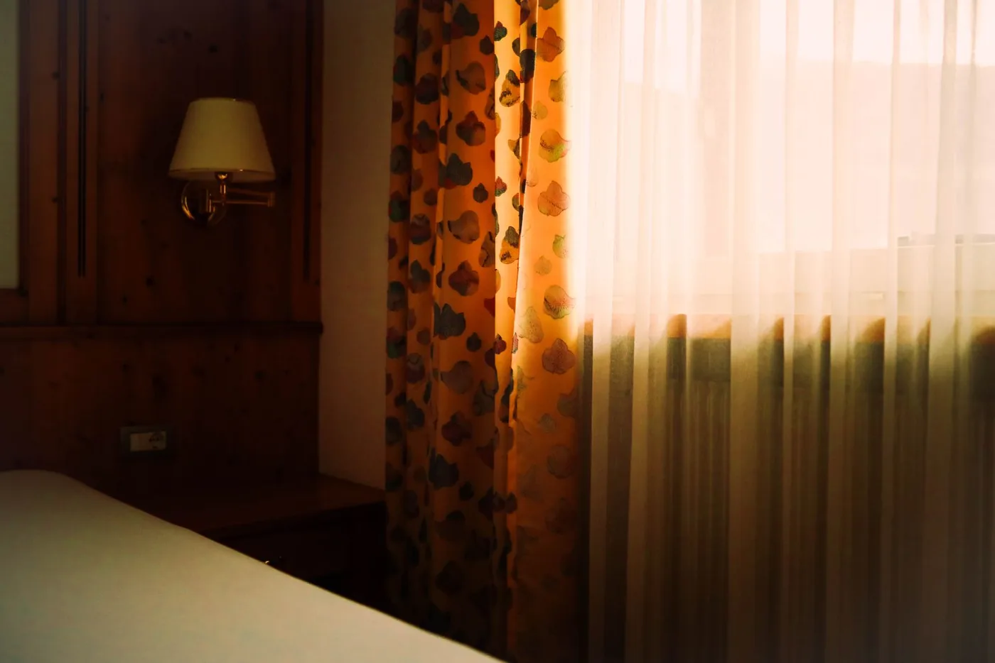 Sunlight passing through a curtained window beside a bed
