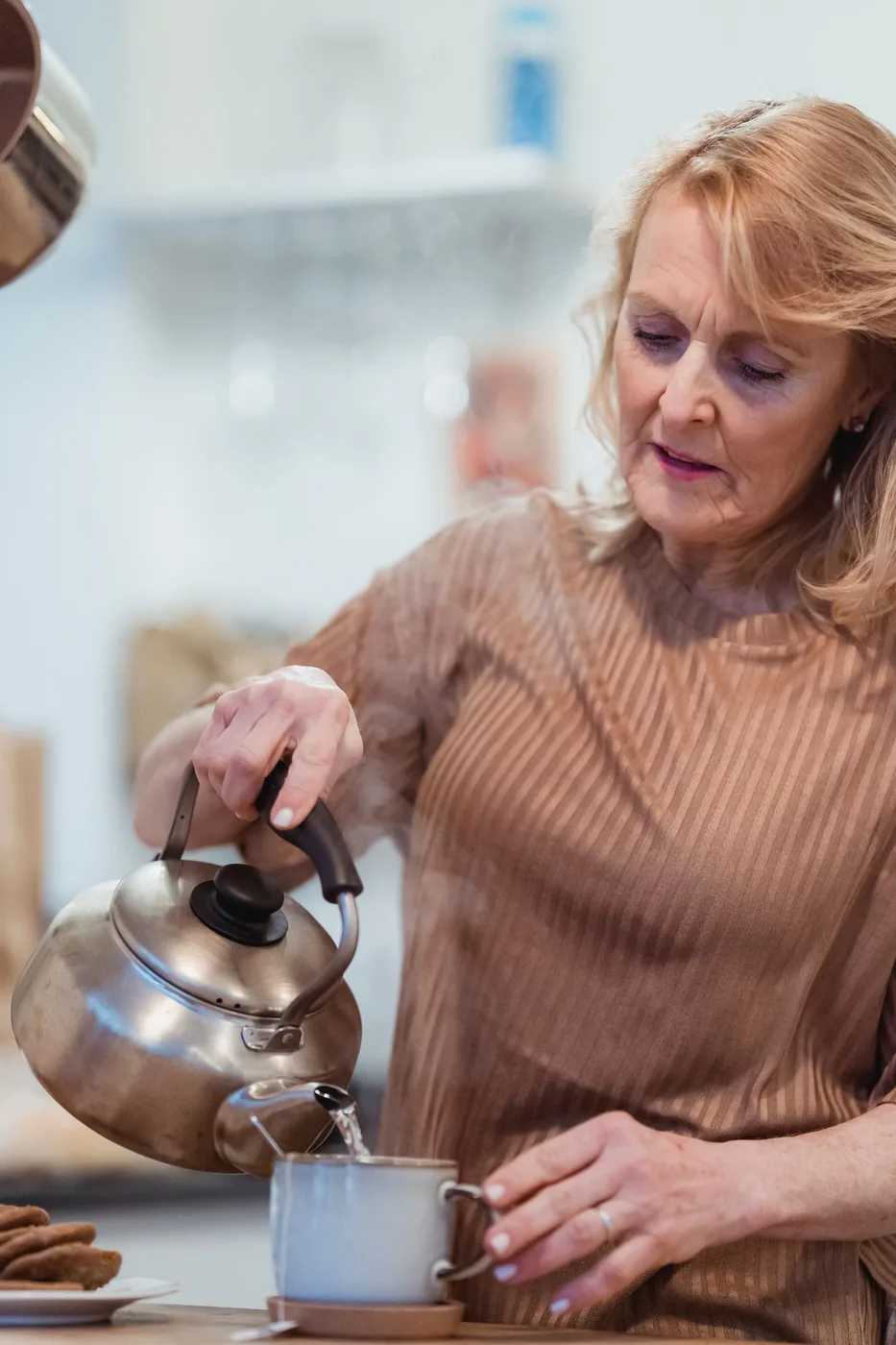 A woman pouring hot water from a kettle into a mug in her kitchen