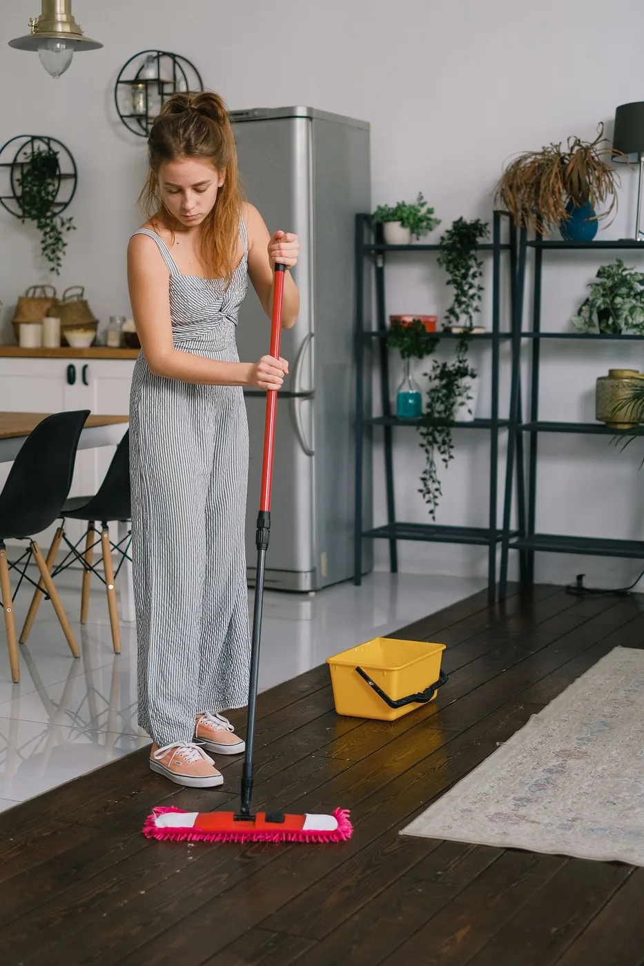 A woman using a mop to clean the wooden floor of a home kitchen